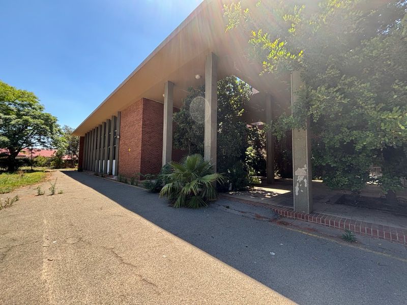 Exterior view of an office building featuring a brick facade, covered walkway with concrete pillars, and an adjacent asphalt driveway.