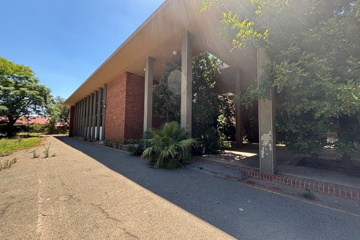 Exterior view of an office building featuring a brick facade, covered walkway with concrete pillars, and an adjacent asphalt driveway.