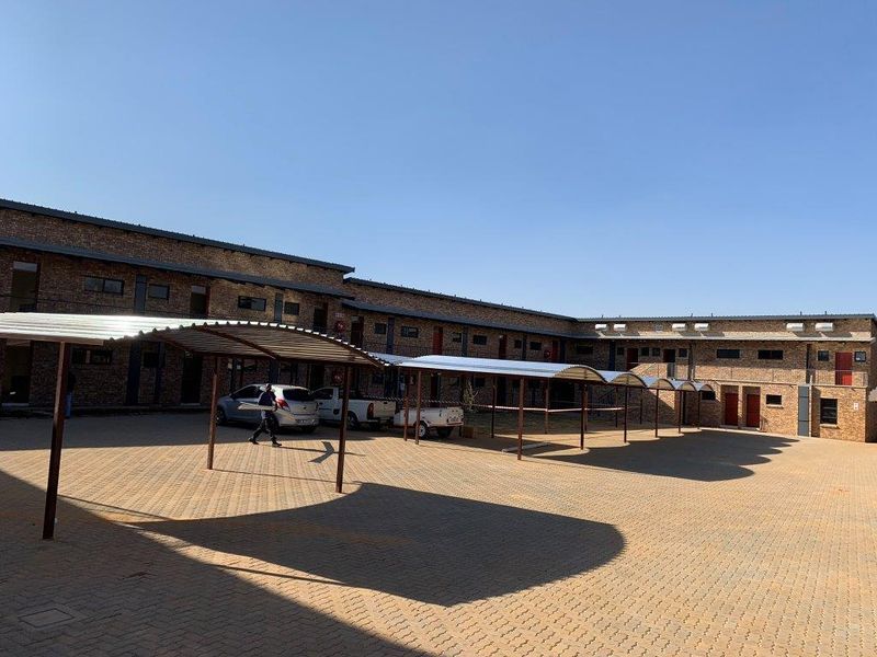 Exterior view of an apartment complex featuring a large paved courtyard with covered parking bays and exposed brick building facades.