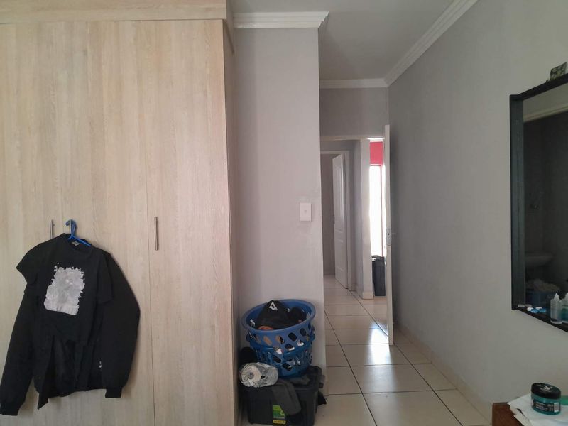 A bedroom featuring built-in wardrobes, tiled flooring, and neutral wall finishes, with a view leading into an adjacent hallway.