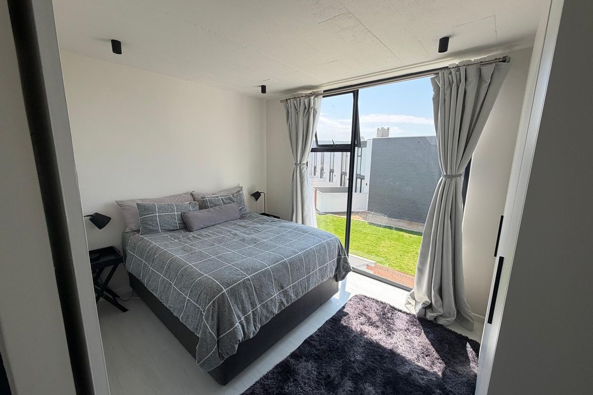 A bright bedroom featuring an exposed concrete ceiling, recessed spotlights, and a large floor-to-ceiling window with views of the surrounding area.