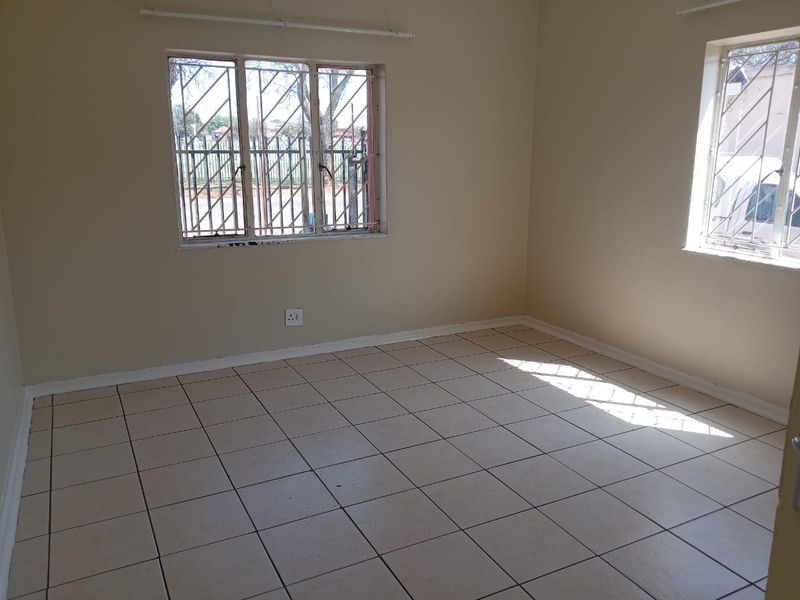 An empty bedroom featuring tiled flooring and windows fitted with security bars, offering a neutral canvas for personalization.