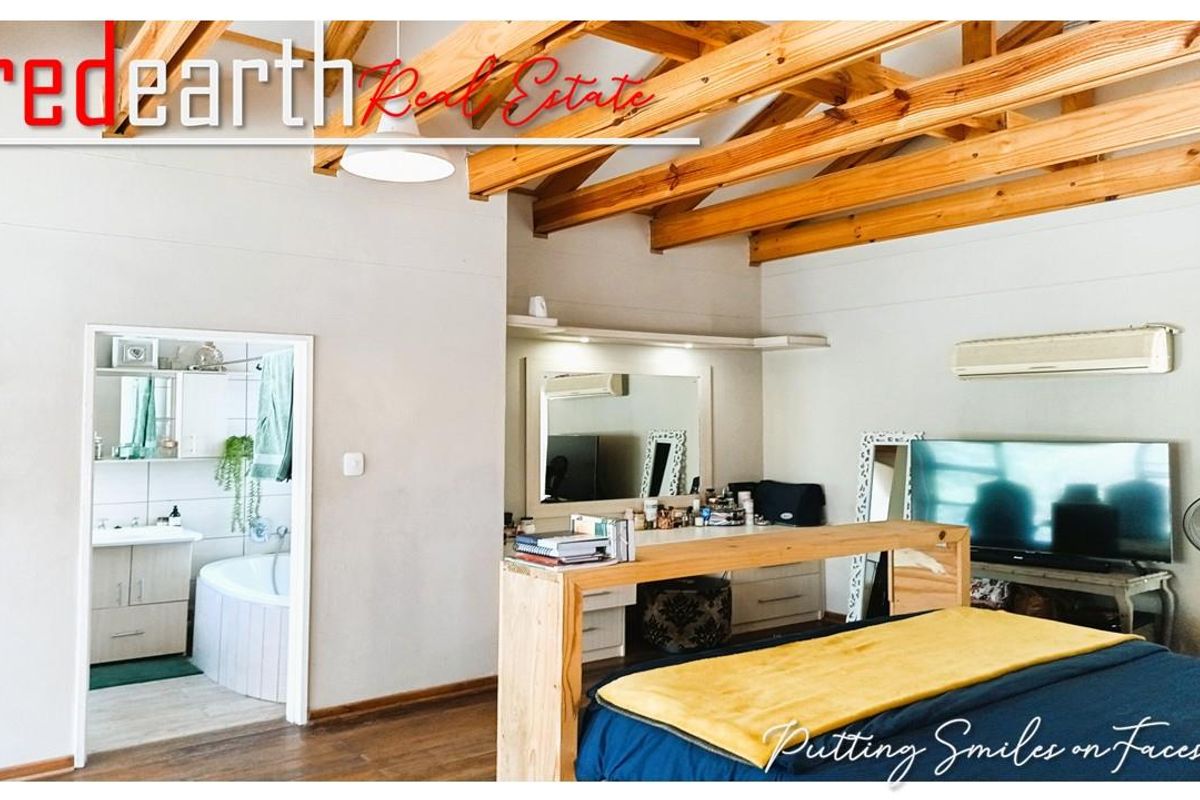 Spacious bedroom featuring exposed timber roof trusses, an integrated air conditioning unit, and an adjoining en-suite bathroom with a built-in vanity and bathtub.