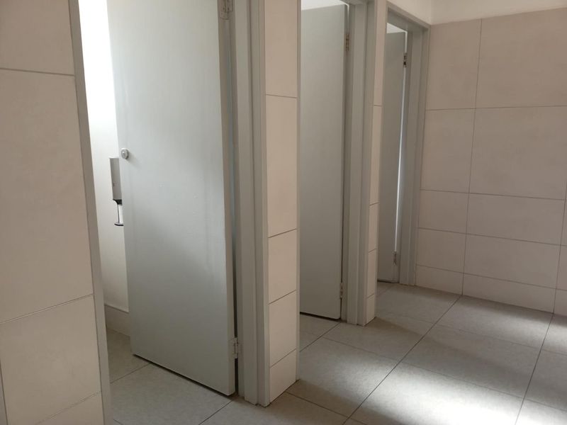 A clean, functional office bathroom area featuring tiled walls, tiled flooring, and multiple private cubicle doors.