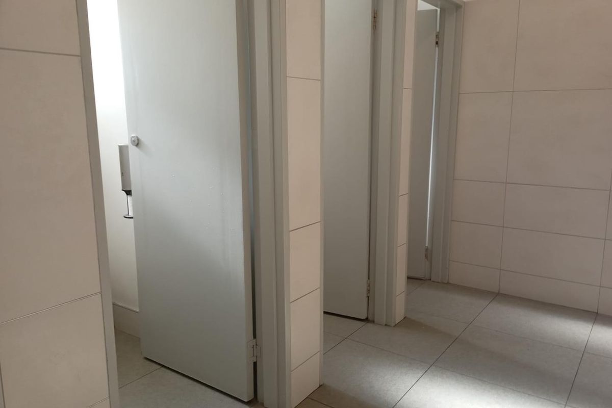 A clean, functional office bathroom area featuring tiled walls, tiled flooring, and multiple private cubicle doors.