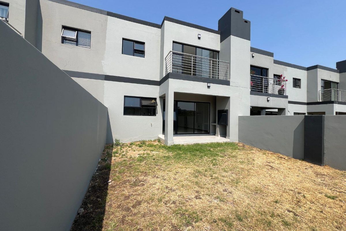 Rear view of a modern cluster home featuring a private garden, a covered patio with a built-in braai, and an upper-level balcony.