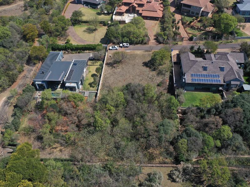 Aerial view of a vacant residential plot situated between two established properties, featuring mature trees and natural vegetation.
