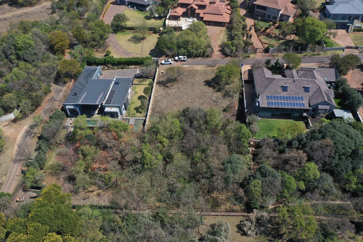 Aerial view of a vacant residential plot situated between two established properties, featuring mature trees and natural vegetation.