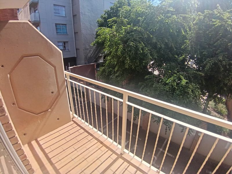 A functional apartment balcony featuring tiled flooring and a metal safety balustrade, overlooking a leafy outdoor area.