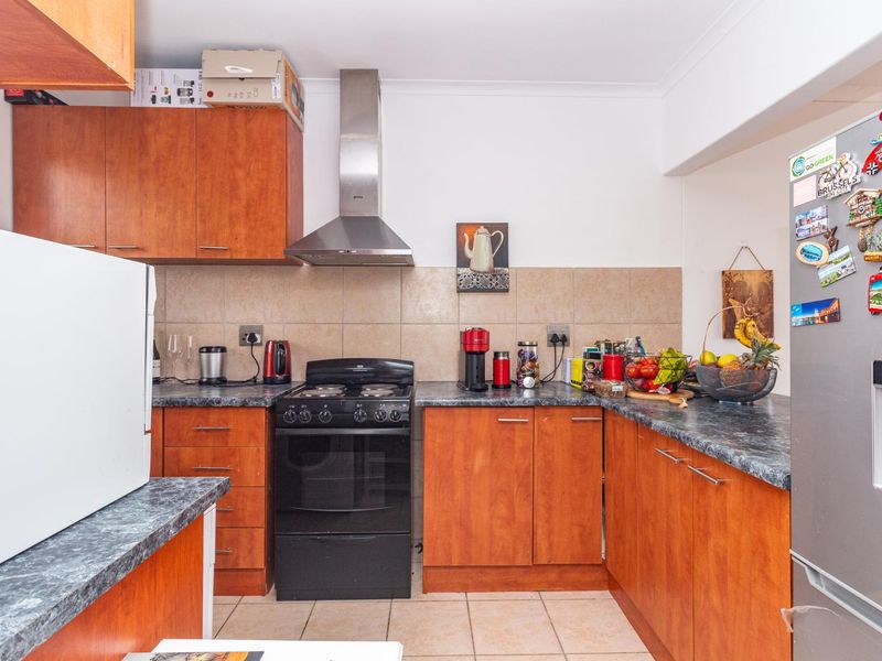 A functional kitchen featuring wooden cabinetry, laminate countertops, a tiled backsplash, and a stainless steel extractor fan.
