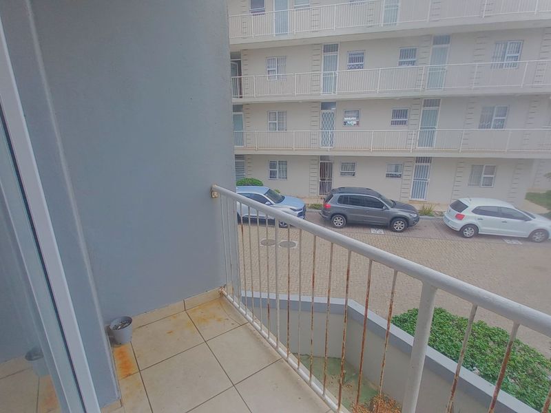 A balcony featuring tiled flooring and a metal balustrade, overlooking the apartment complex parking area.