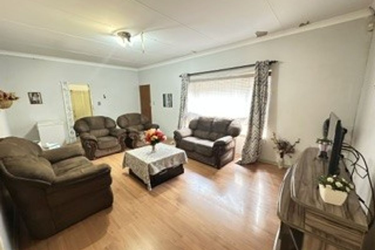 A spacious living room featuring laminate flooring and coved ceilings, offering a comfortable area for relaxation and family gatherings.