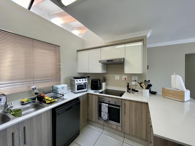 Modern kitchen featuring sleek two-tone cabinetry, stone countertops, integrated appliances, and a bright skylight, offering a functional and contemporary cooking space.