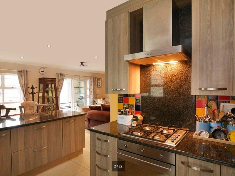 Open-plan kitchen featuring granite countertops, built-in gas hob, and stainless steel extractor, flowing into a living area with access to outdoor space.