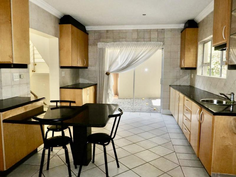 A functional kitchen featuring light wood cabinetry, dark granite countertops, tiled flooring, and direct access to an outdoor patio area through sliding glass doors.