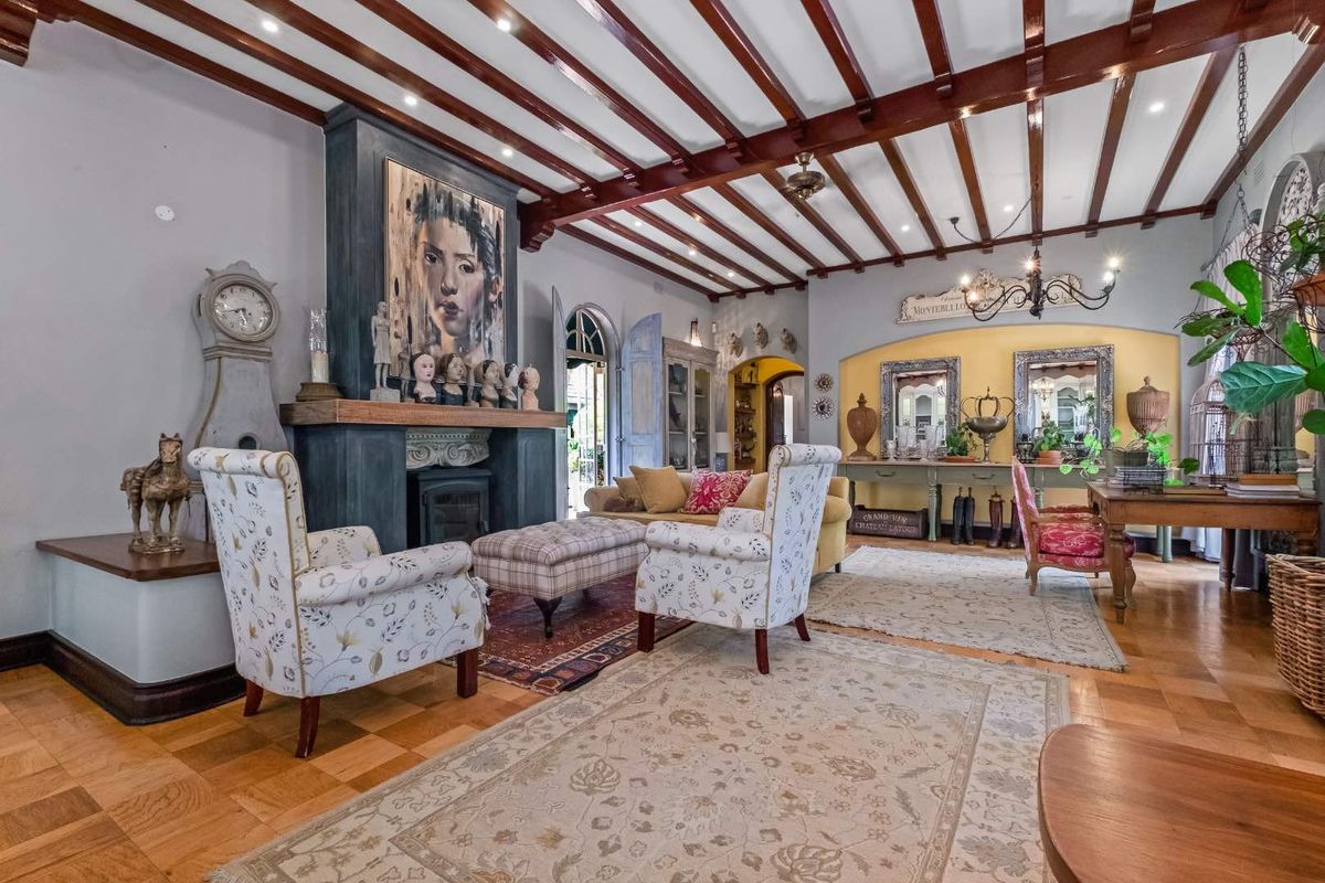 Spacious living room featuring exposed timber ceiling beams, elegant parquet flooring, and a prominent fireplace with a decorative mantelpiece.