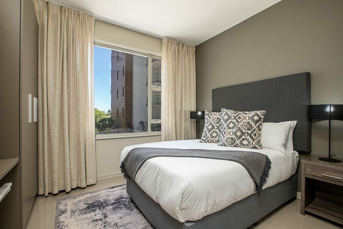A well-maintained bedroom featuring tiled flooring, a large window with natural light, and a built-in wardrobe.