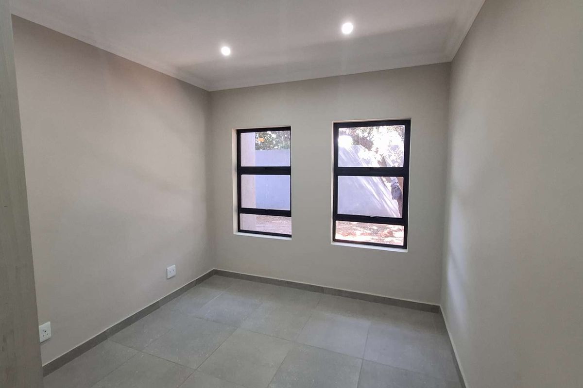 A clean, empty bedroom featuring neutral wall paint, modern tiled flooring, and dual aluminium-framed windows with recessed downlighting.