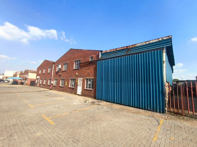 Industrial property exterior featuring a combination of brick and corrugated metal cladding with an adjacent paved parking area.