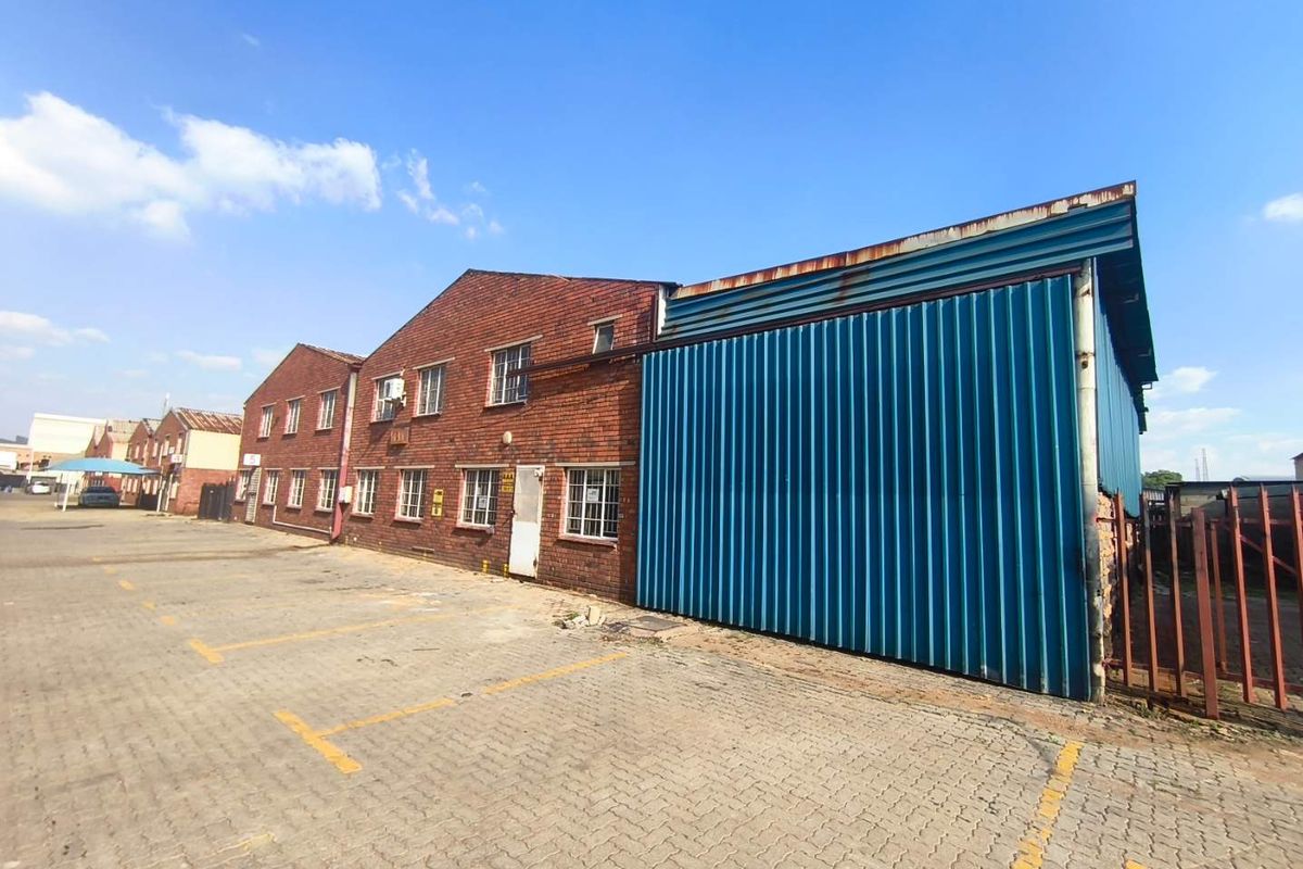 Industrial property exterior featuring a combination of brick and corrugated metal cladding with an adjacent paved parking area.