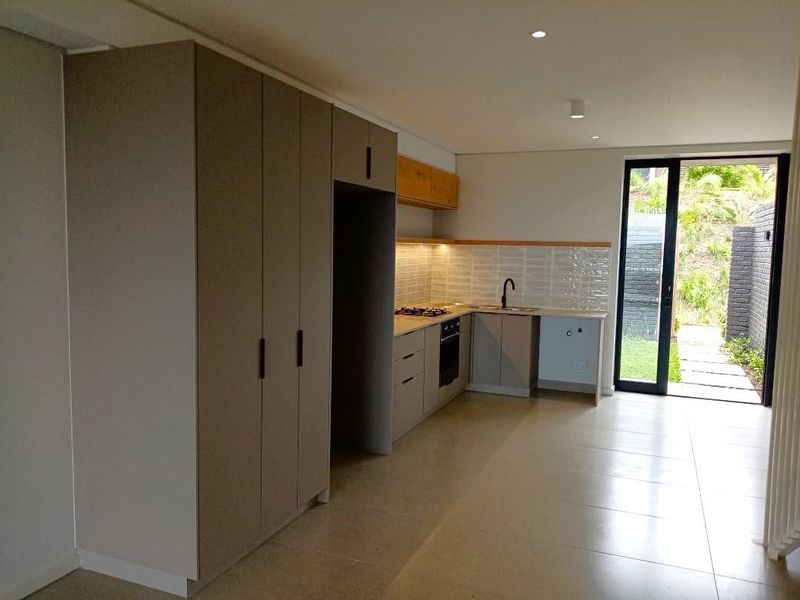Modern kitchen featuring sleek built-in cabinetry, gas hob, oven, and subway tile backsplash, with direct access to a private outdoor area.