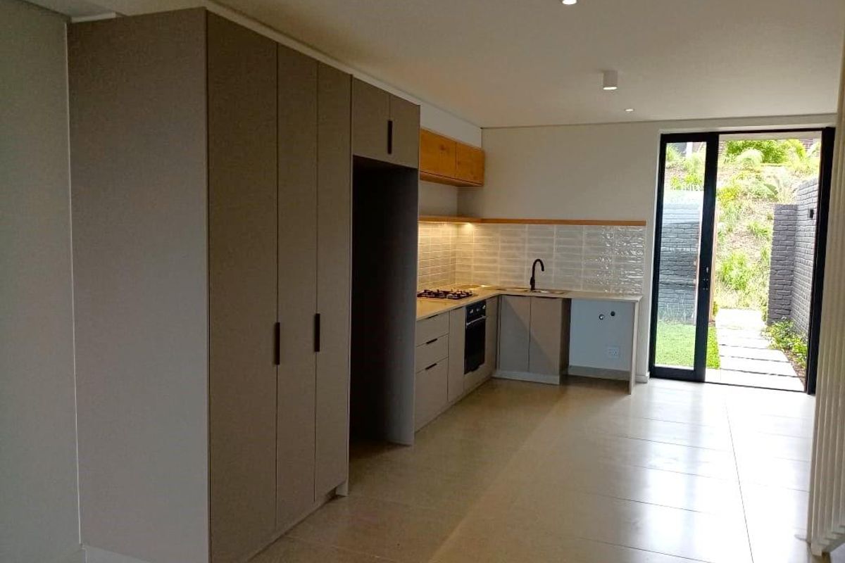 Modern kitchen featuring sleek built-in cabinetry, gas hob, oven, and subway tile backsplash, with direct access to a private outdoor area.