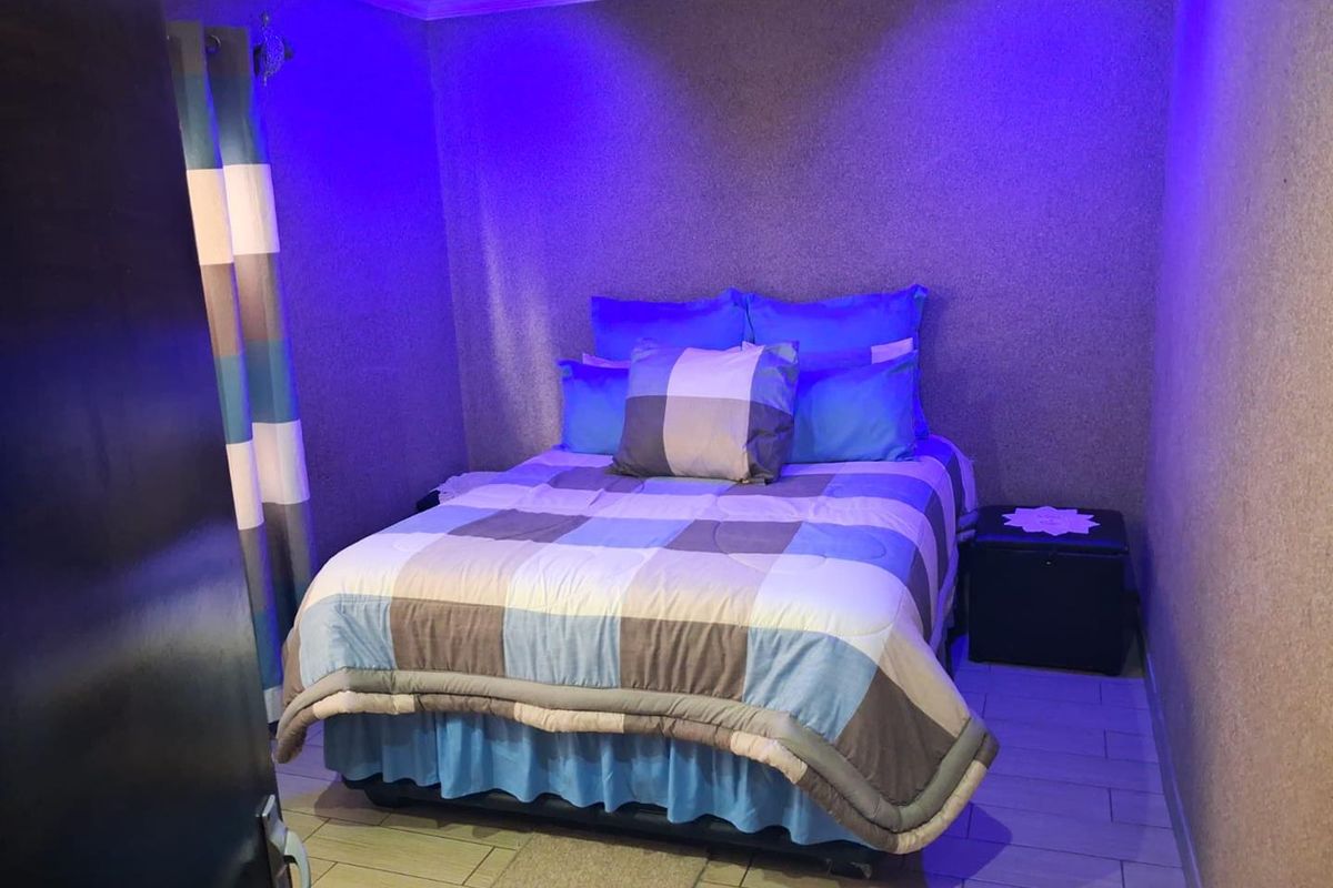 A compact bedroom featuring tiled flooring and recessed ceiling lighting, currently styled with blue accent lighting.