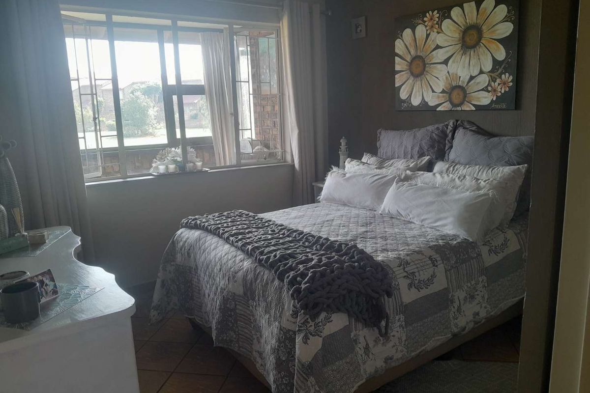 A cozy bedroom featuring tiled flooring and a large window with security bars, providing natural light and a view of the exterior.
