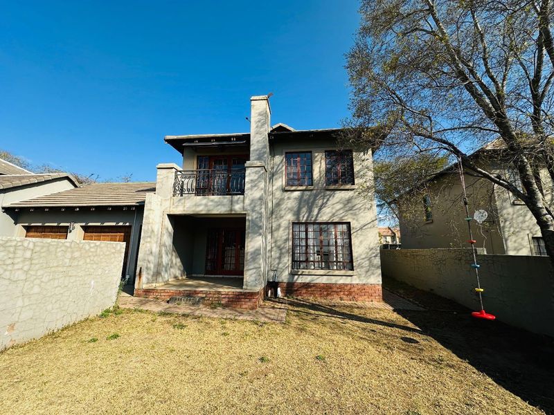 Rear view of the townhouse featuring a balcony with wrought iron railing, a chimney, and a paved patio area leading to the garden.