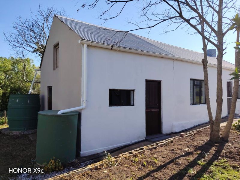 Rear exterior view of the property featuring a corrugated metal roof, rainwater collection tanks, and established trees in the garden area.