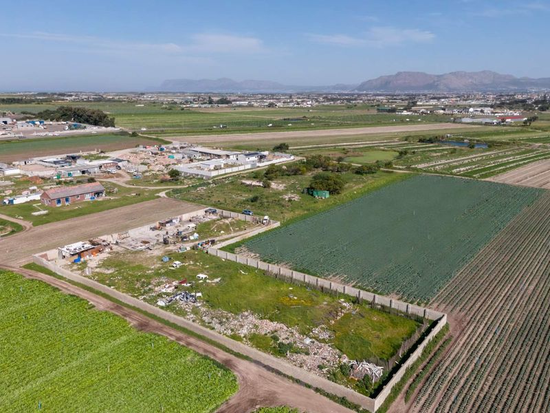 Aerial view of a vacant residential plot featuring perimeter walling, situated in a rural agricultural landscape with mountain views.