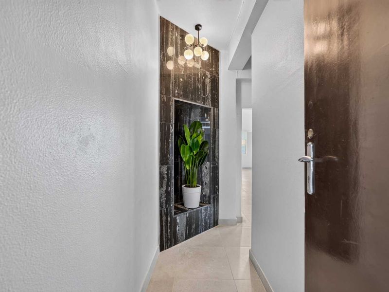 A bright, modern hallway featuring a striking marble-clad built-in wall niche and contemporary pendant lighting, leading into the main living area.
