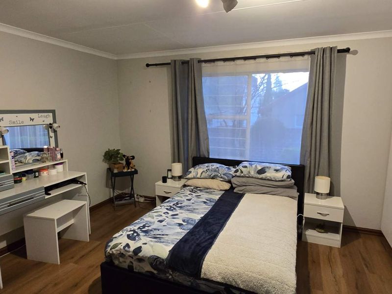A well-maintained bedroom featuring laminate flooring, neutral wall finishes, and ample storage with built-in cupboards.