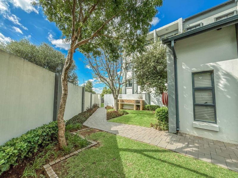 A well-maintained private garden area featuring a paved walkway, manicured lawn, perimeter boundary walls, and a built-in brick braai facility.