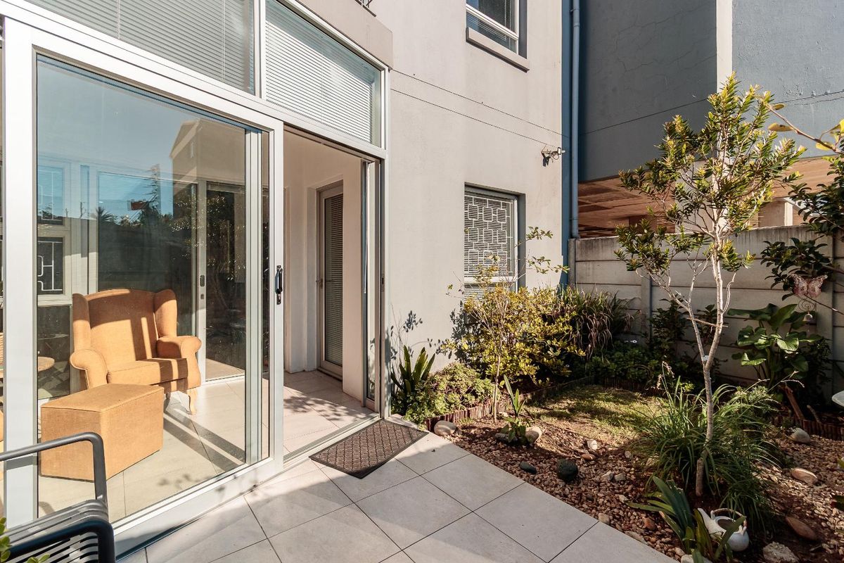A private rear courtyard featuring a tiled patio area, sliding glass door access to the interior, and a landscaped garden with a boundary wall.
