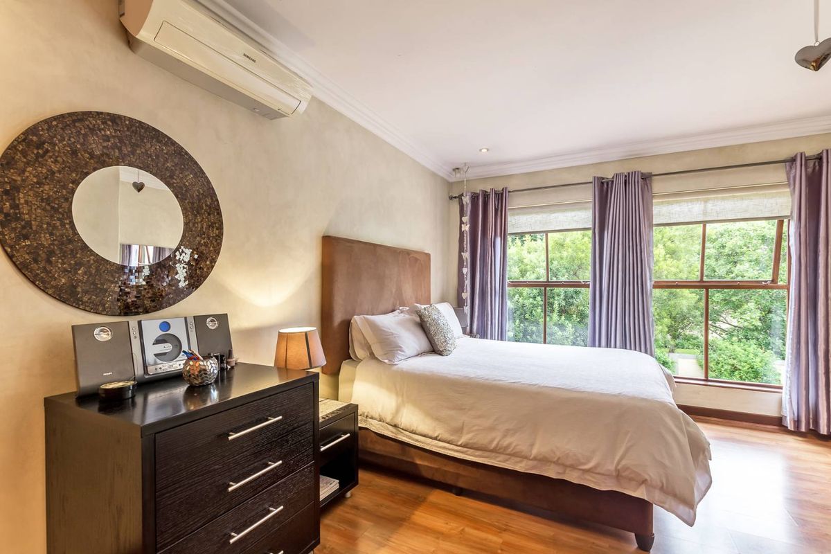 A well-maintained bedroom featuring timber flooring, large windows with garden views, and a wall-mounted air conditioning unit.