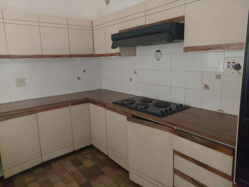 A dated kitchen featuring built-in cabinetry, laminate countertops, an electric hob, and an extractor fan, offering potential for a modern renovation.