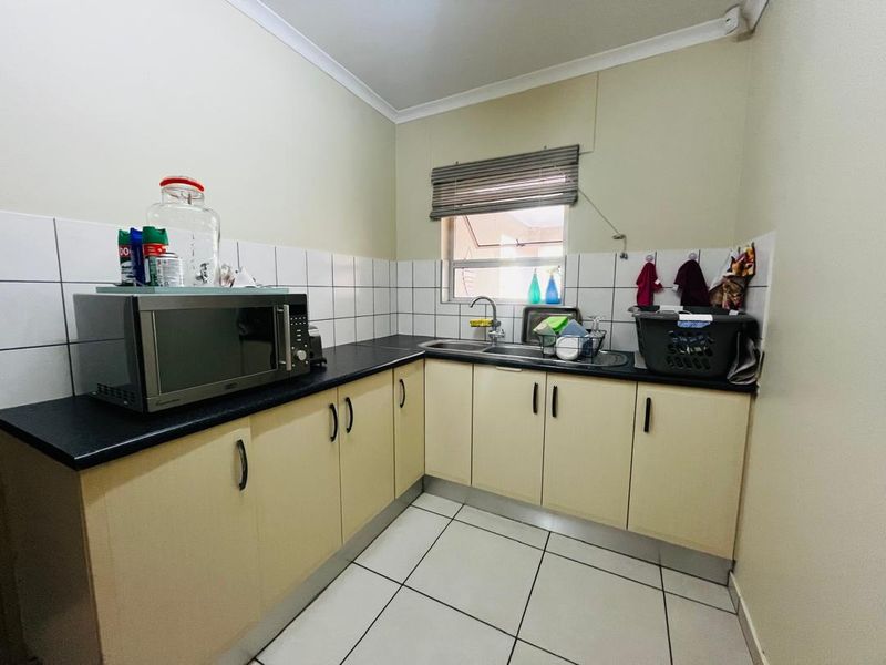 A functional scullery featuring laminate countertops, a stainless steel double sink, tiled splashback, and ample built-in cabinetry for storage and prep.