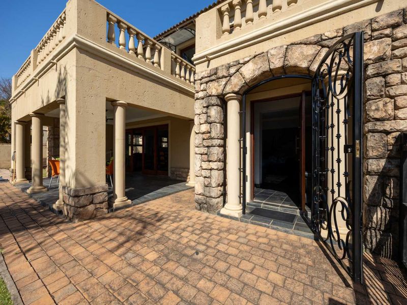 A well-maintained rear exterior featuring stone cladding, a paved patio area, classic columns, and an arched entrance with a decorative wrought iron gate.
