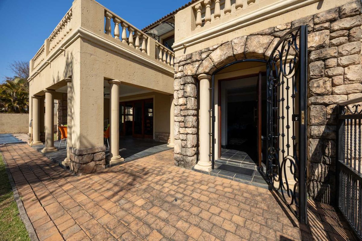 A well-maintained rear exterior featuring stone cladding, a paved patio area, classic columns, and an arched entrance with a decorative wrought iron gate.