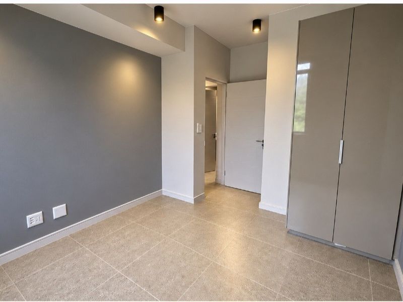 A modern, empty bedroom featuring neutral grey walls, tiled flooring, and a sleek built-in wardrobe with recessed ceiling lighting.