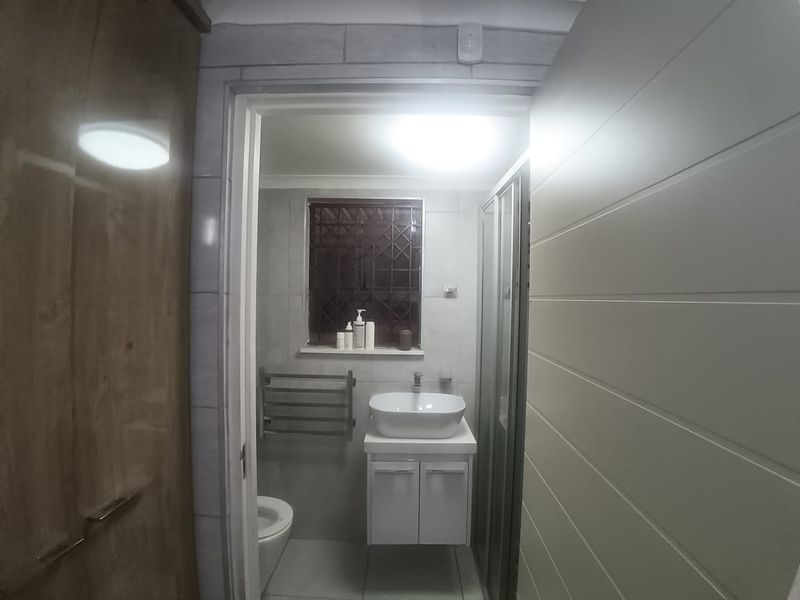 A compact bathroom featuring a modern vessel sink with vanity, a shower enclosure, and a heated towel rail, finished with neutral wall and floor tiles.