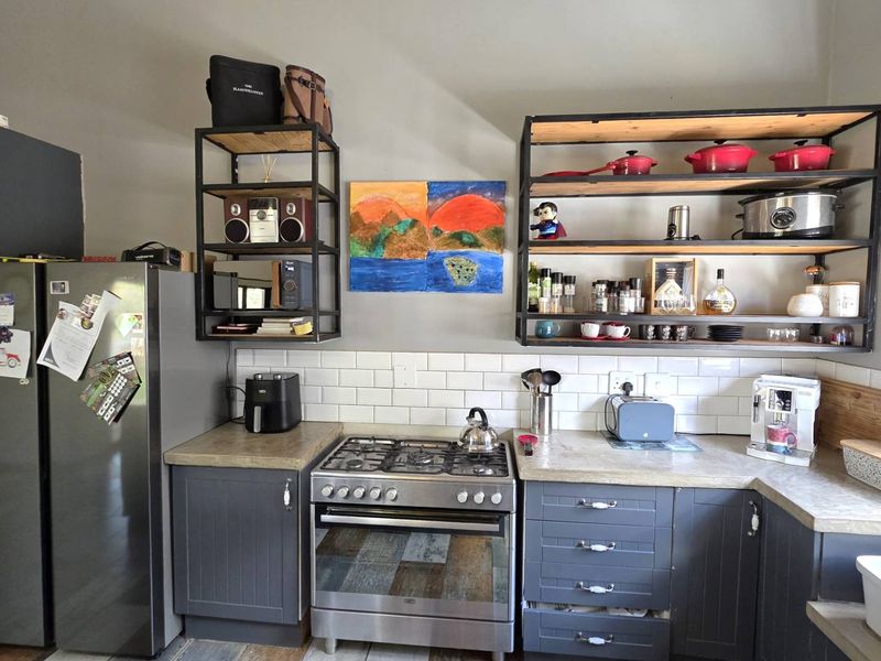 A well-appointed kitchen featuring dark grey cabinetry, subway tile backsplash, open industrial-style shelving, a gas stove, and a classic apron-front sink.