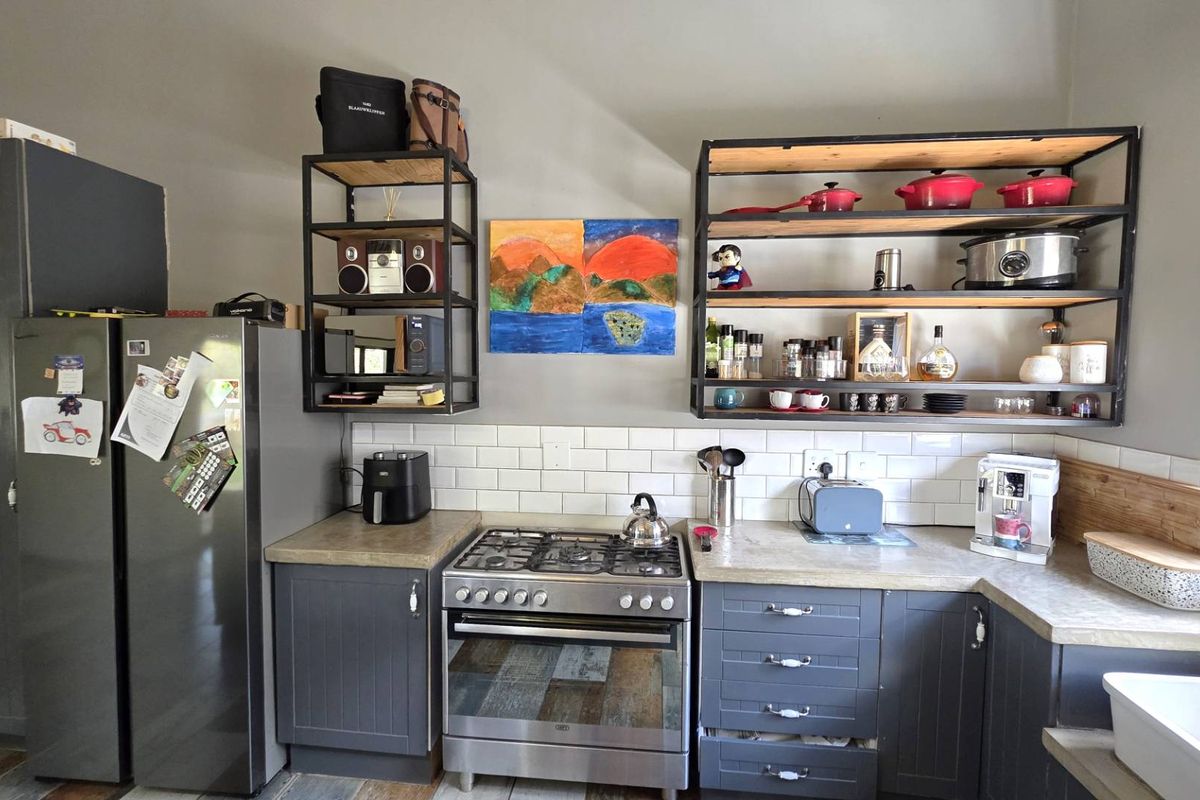 A well-appointed kitchen featuring dark grey cabinetry, subway tile backsplash, open industrial-style shelving, a gas stove, and a classic apron-front sink.