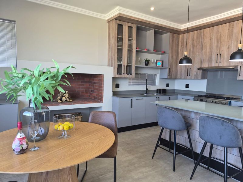 Modern open-plan kitchen featuring wood-grain cabinetry, stone countertops, a central island, and a built-in brick fireplace, creating a cohesive living and dining space.