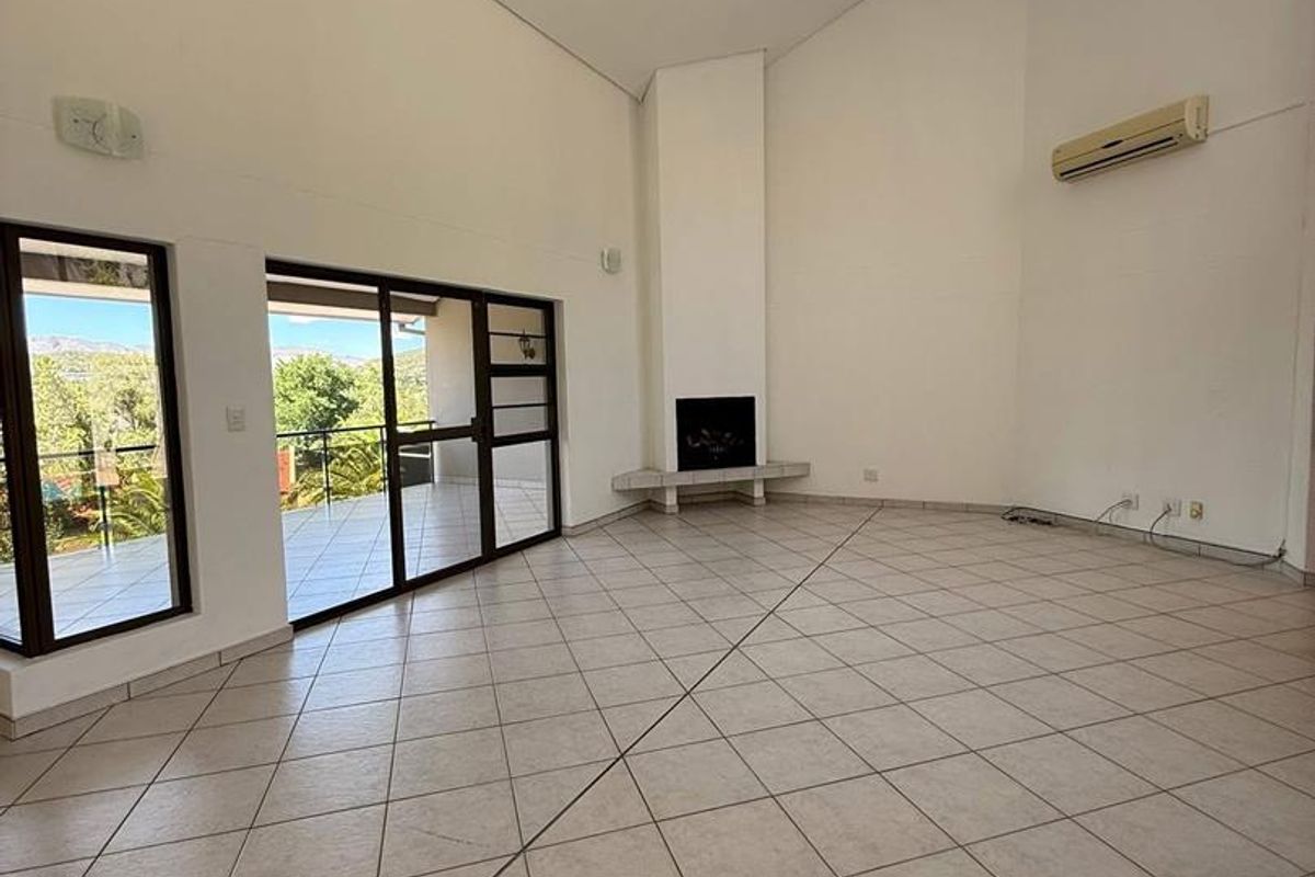 Spacious living area featuring high vaulted ceilings, a built-in fireplace, tiled flooring, and large glass sliding doors leading to an outdoor patio.