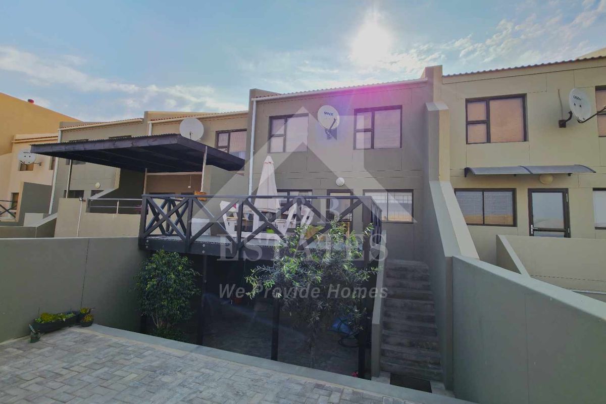 Rear view of the townhouse featuring a raised timber deck, concrete staircase, and a paved courtyard area with boundary walls.