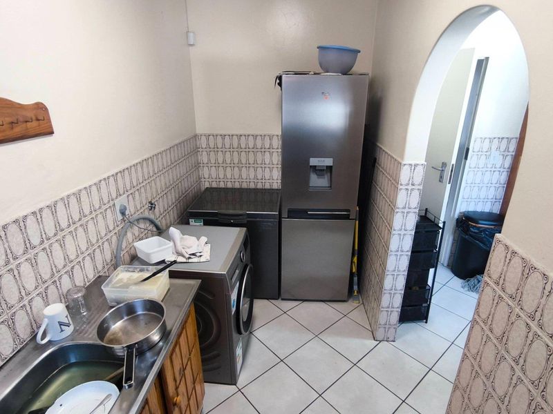A functional laundry area featuring tiled splashbacks, a stainless steel sink, and tiled flooring, providing a practical space for utility and washing tasks.