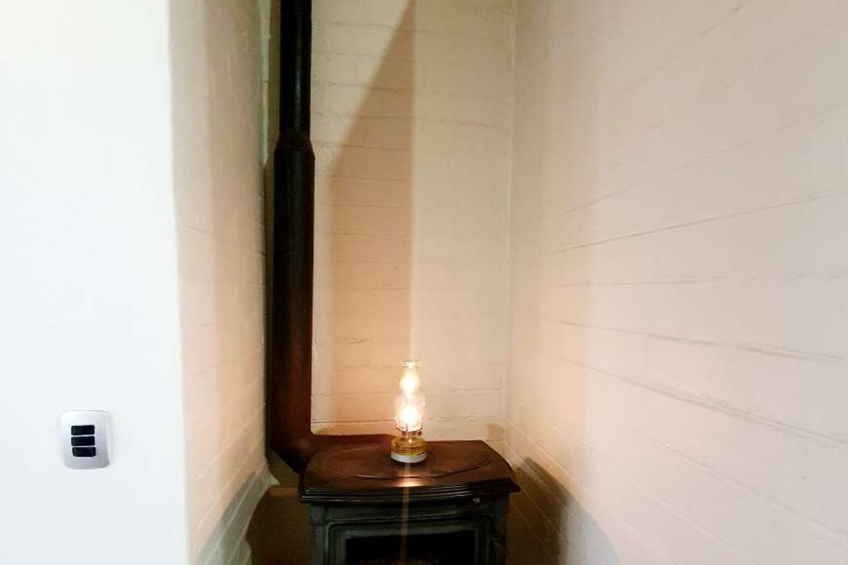A cozy corner featuring a cast-iron wood-burning stove with a vertical flue pipe, set on a raised hearth against painted brick walls.