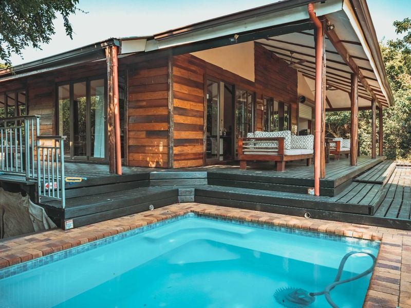 A well-maintained timber-clad home featuring a spacious covered deck area overlooking a private swimming pool with brick coping.